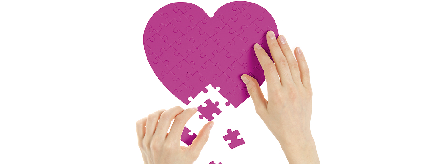 Herz-Puzzle in Magenta, das von zwei Händen zusammengesetzt wird
